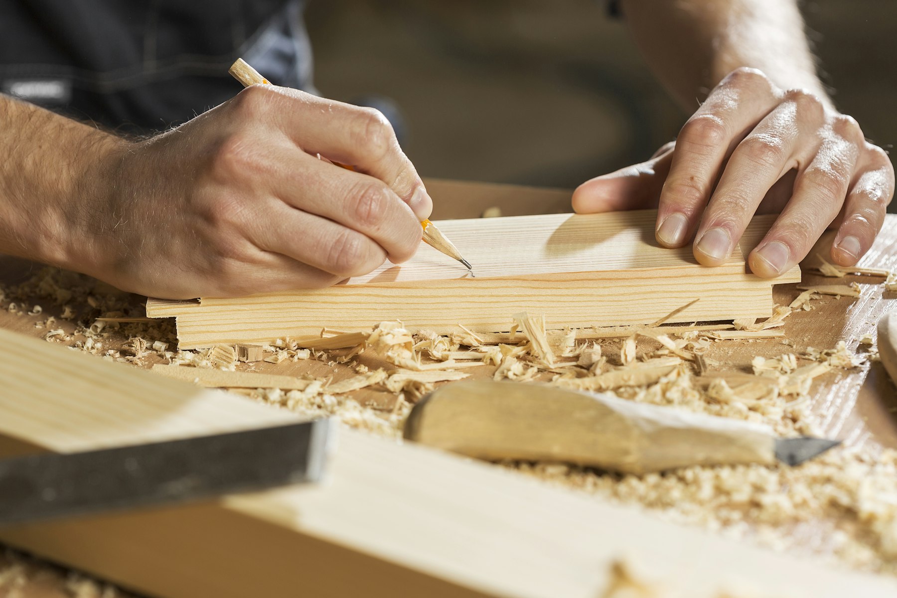 Mani di un falegname che tracciano le misure su una tavola di legno